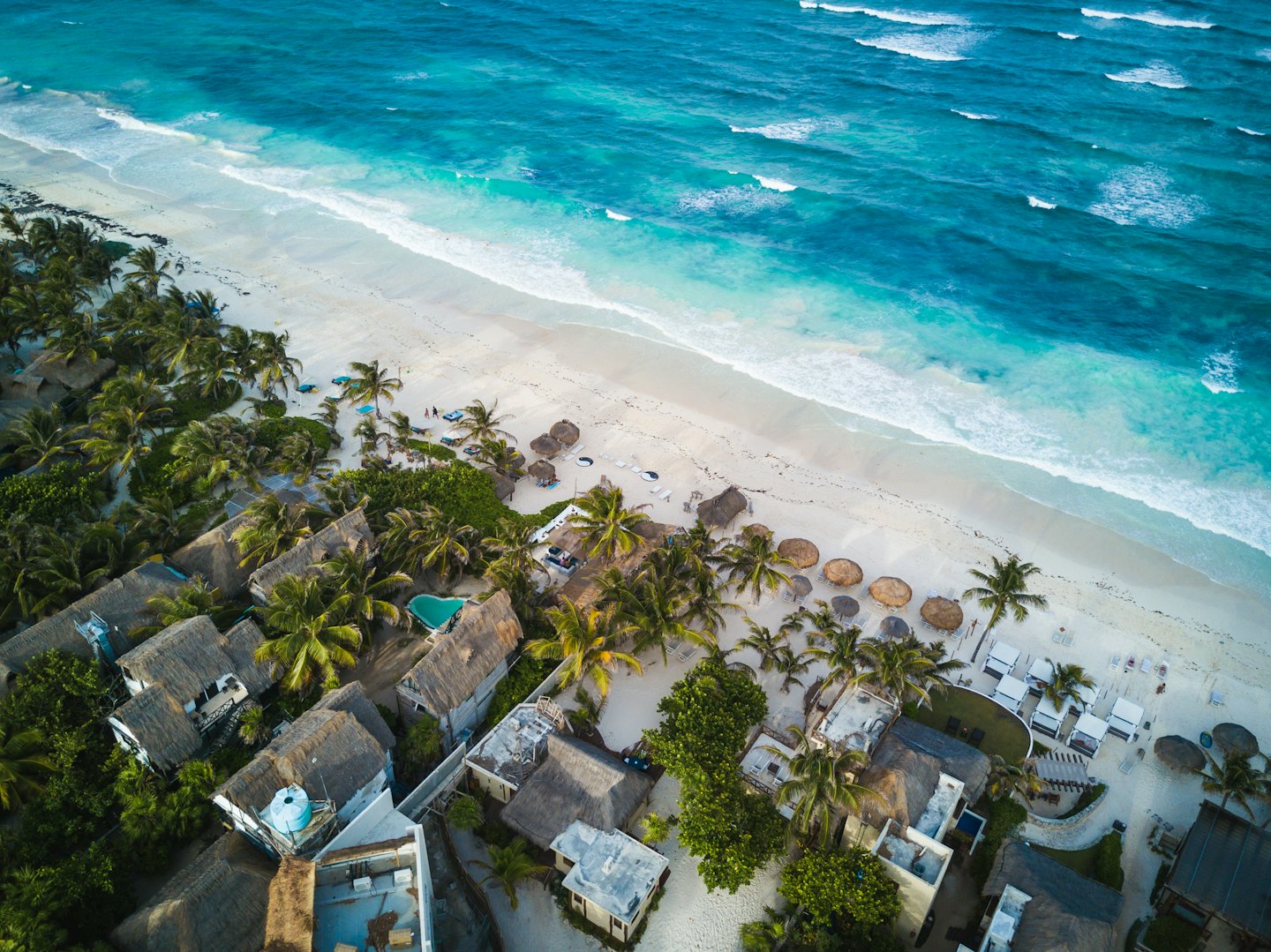 Resort tropical con bungalows de techo de paja en playa de arena blanca.